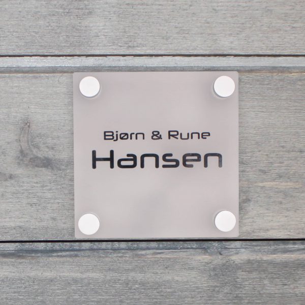 Fotografi av et frostet dørskilt på en grå vegg. På dørskiltet står det "Bjørn & Rune Hansen" i sort skrift.